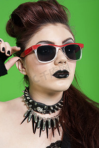 墨镜模特摄影照片_绿色背景中戴墨镜的年轻朋克女子的特写