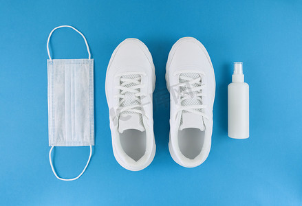 运动鞋背景图摄影照片_蓝色背景上的白色医用口罩、运动鞋和洗手液。