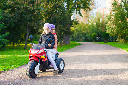 绿色公园里骑着儿童摩托车的可爱小女孩