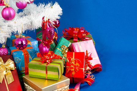 装饰礼物盒摄影照片_白色常青树下的圣诞礼物堆