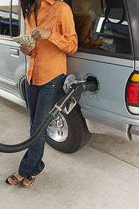 女人在加油站靠在汽车上数钱的低部分