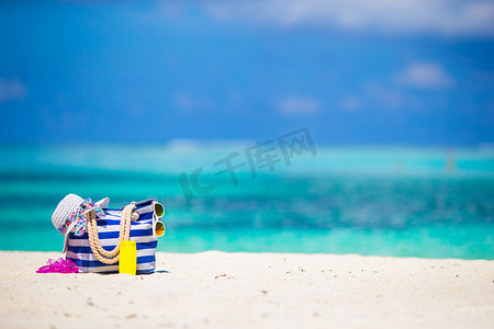 白色海滩上的条纹包、蓝色毛巾、太阳镜、防晒霜瓶和泳衣