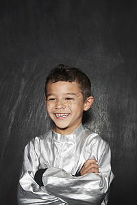 黑色背景下，身穿银色服装、双臂交叉的微笑小男孩的肖像