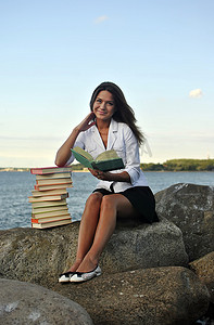 坐在海边岩石上拿着书的女孩
