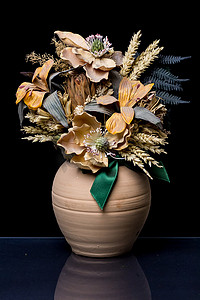 黑色背景上带绿色丝带的赤土陶器花瓶中的花卉组合物