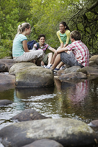 十几岁的男孩和女孩坐在森林河边的石头上
