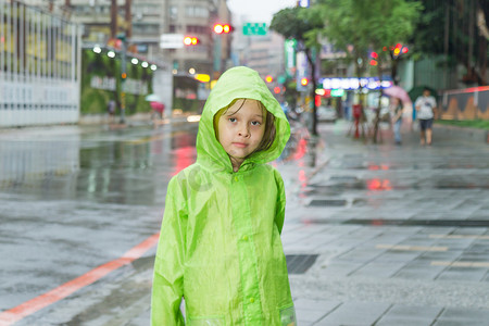 穿着绿色雨衣站在雨中的小女孩