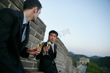 两位中外商务人士在长城上端酒杯交谈