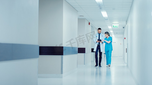 医生和女医生在医院的走廊里走来走去，一边谈论病人的健康，一边查阅数码平板电脑。配备专业人员的现代明华医院.
