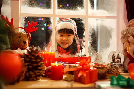 可爱礼物盒子摄影照片_小女孩透过窗户看圣诞节礼物
