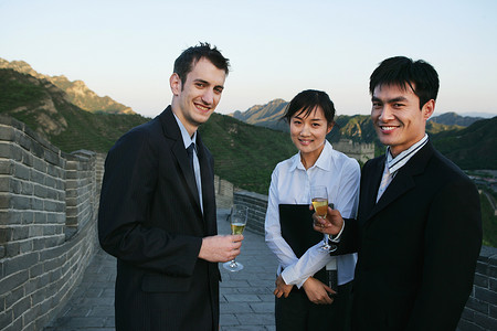 三位中外商务人士在长城上端酒杯站立