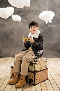 行李箱男孩摄影照片_小男孩坐在复古行李箱上玩游戏机