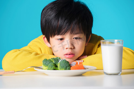 蓝色小学摄影照片_盯着蔬菜发愁的小男孩