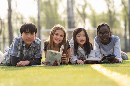 认真学习的男孩摄影照片_可爱的小学生们趴在草地上看书