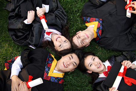 四个身穿学士服的大学生躺在草地上
