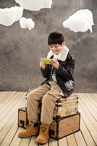 创意游戏机摄影照片_小男孩坐在复古行李箱上玩游戏机