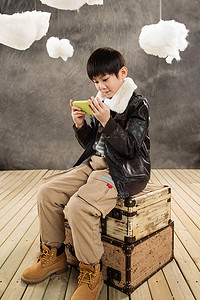 小男孩坐在复古行李箱上玩游戏机