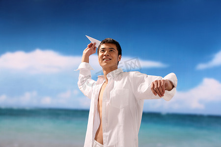 白色的纸飞机摄影照片_东方男人在海滩扔纸飞机