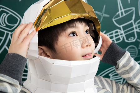 思考插画摄影照片_戴着航天员头盔的小男孩站在黑板前