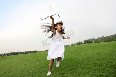 一个东方女孩在草上玩飞机模型