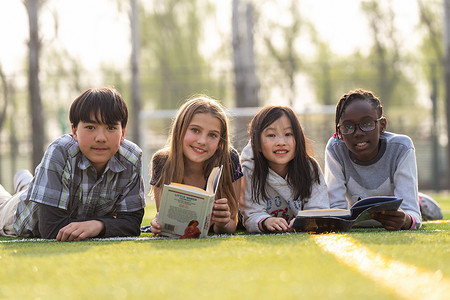 可爱女生微笑摄影照片_可爱的小学生们趴在草地上看书