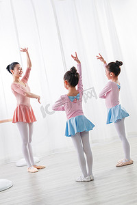 儿童表演摄影照片_年轻舞蹈老师教小女孩们跳芭蕾