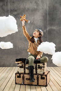 木质飞机模型摄影照片_坐在行李箱上的女孩举着飞机模型