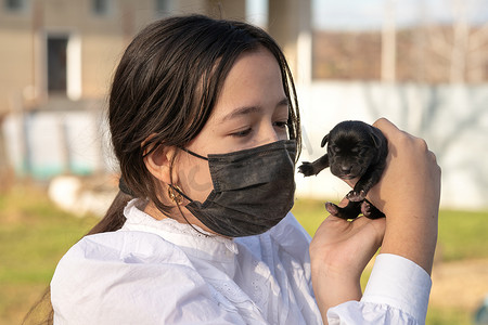 温柔摄影照片_一个戴着防护面具的女孩抱着一只新生的拉布拉多犬。爱。温柔的概念。第一天的生活.