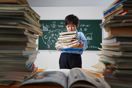 学生抱着课本摄影照片_搬着沉重课本的小学男生