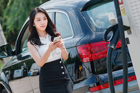 加油摄影照片_青年女人使用手机自助充电汽车