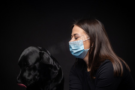 拍摄影棚摄影照片_一个拉布拉多猎犬的肖像，带着一个保护的医疗面具和一个女主人在一起。这张照片是在摄影棚拍的