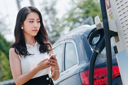 青年女人使用手机自助充电汽车