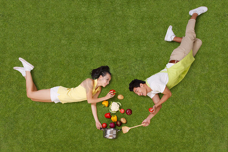俯视俯视锅摄影照片_青年男女拿着蔬菜躺在草地上