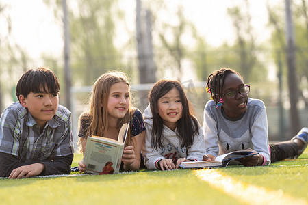 成考教育摄影照片_可爱的小学生们趴在草地上看书
