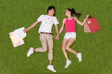 青年男女手提购物袋躺在草地上