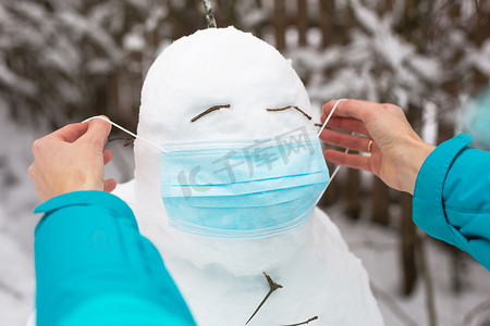 戴着医疗面罩的雪人- -一种新的现实，一种对疾病、感染、兽疫流行中的生命的保护。女人的手戴着雪人面具。冬季家庭户外活动