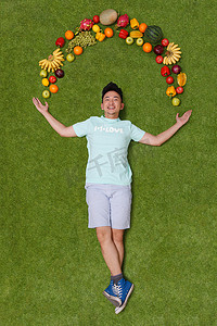 年轻男子躺在草地上手托着水果