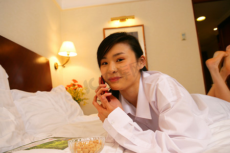 手机容器摄影照片_年轻女士在酒店床上边吃零食边打电话