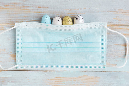 Color quail eggs in face medical mask on wooden background. Coronavirus easter concept