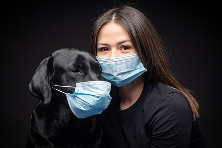 一个拉布拉多猎犬的肖像，带着一个保护的医疗面具和一个女主人在一起。这张照片是在摄影棚拍的