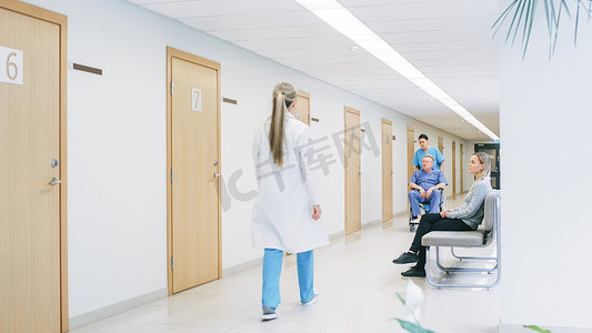 忙碌的医生摄影照片_在医院的走廊里，忙碌的专业人员走过，护士推着轮椅上的老人，病人在等医生。全新医院，配备专业医护人员.