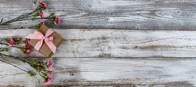 送给母亲节或情人节的真正的粉色康乃馨花和礼物盒在乡村木板的左边 