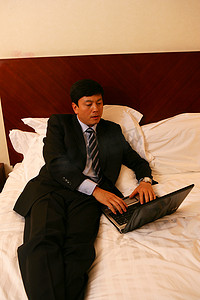 不舒服男摄影照片_商务人士在酒店床上使用笔记本电脑