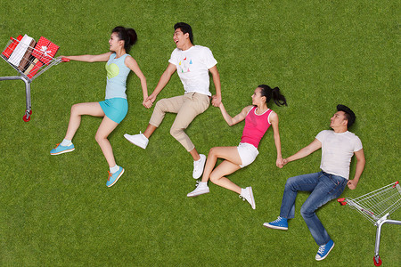 年轻男女在草地上推购物车奔跑