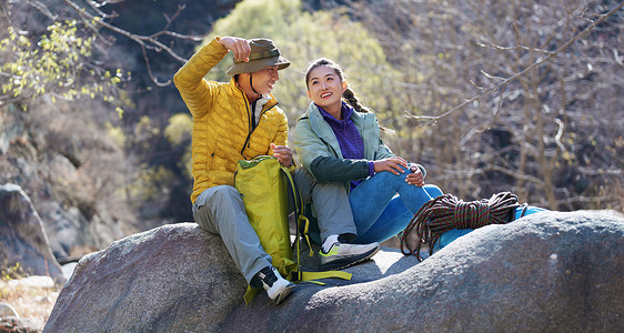 坐在石头摄影照片_徒步旅行的青年伴侣坐在石头上休息