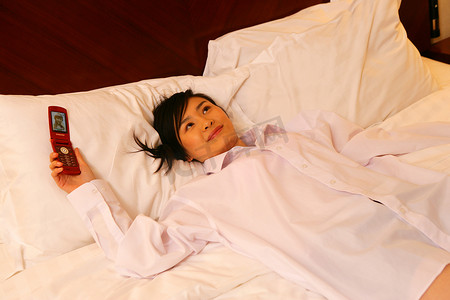 年轻女士拿手机躺在酒店床上
