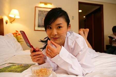 年轻女士在酒店床上边吃零食边发短信