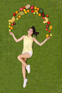 年轻女子手托着水果躺在草地上