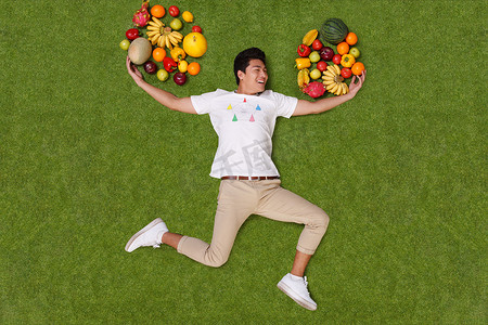 水果新鲜不新鲜摄影照片_年轻男子躺在草地上手托着水果