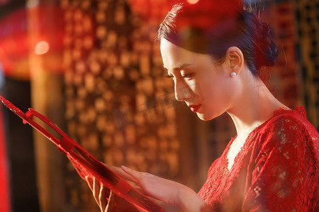 中式剪纸元素摄影照片_站在窗外拿剪纸的青年女人